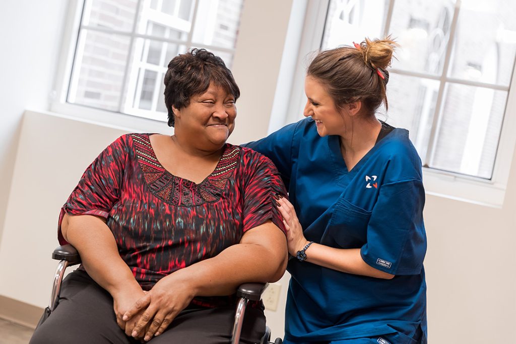 Female nurse interacting with female patient in a wheelchair.