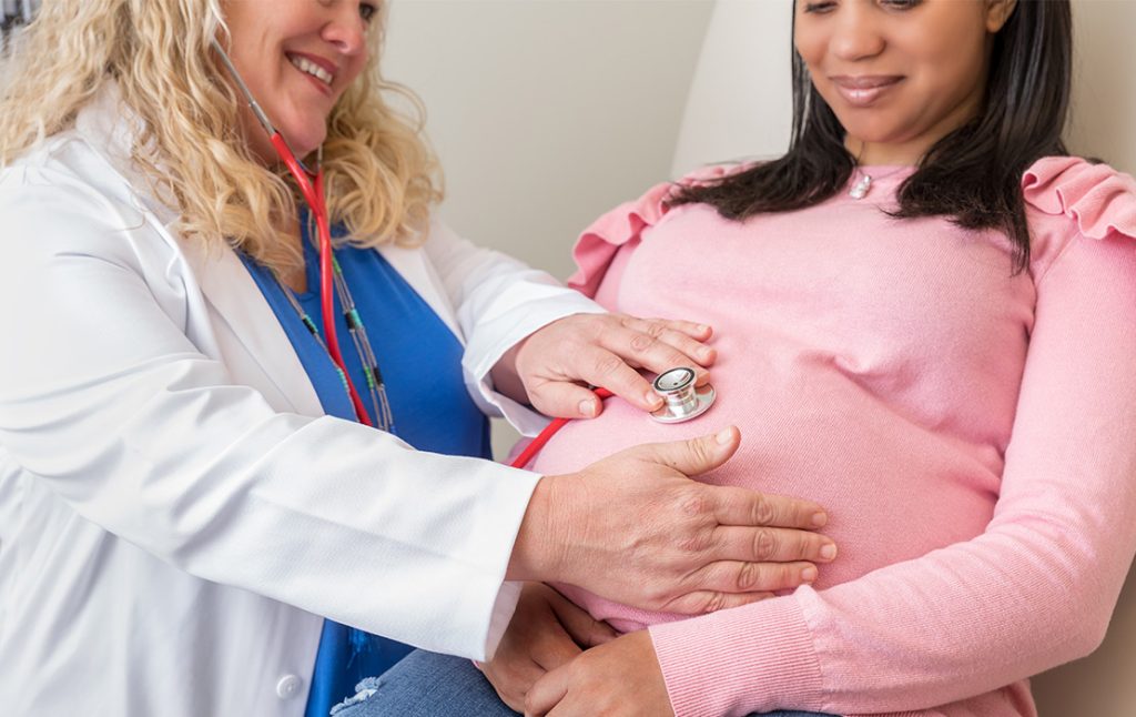 Female Pediatric and Women's Health doctor checking heartbeat of pregnant woman's baby in the womb.