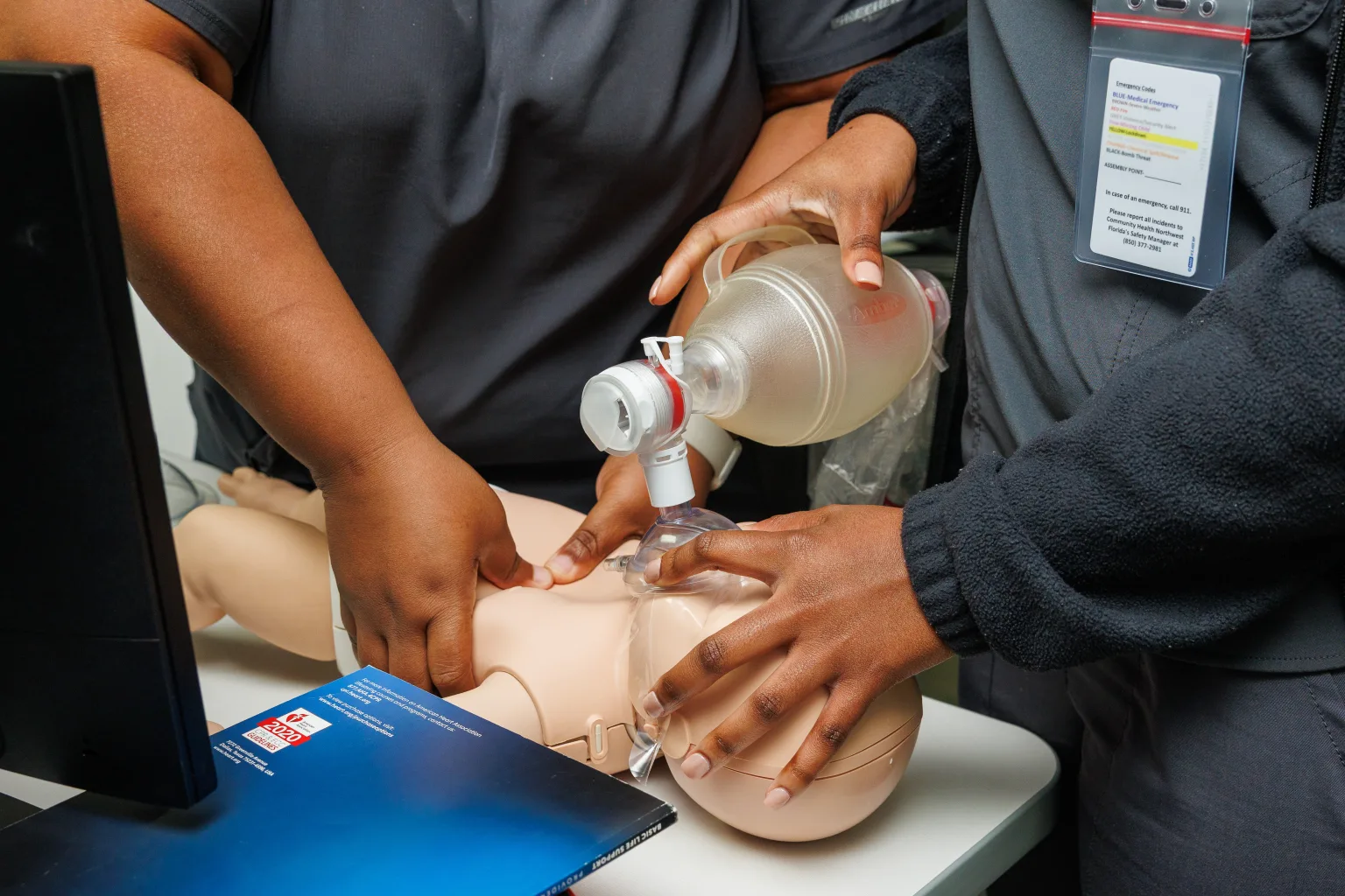 Two women perform CPR and rescue breathing on an infant mannequin.